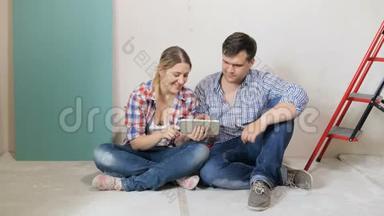 一对年轻夫妇坐在正在装修的新房子的地板上，用互联网选择家具